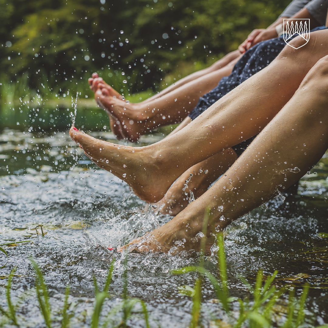 Kuvassa henkilöitä istuu laiturilla ja heiluttelee jalkoja luonnon vedessä.