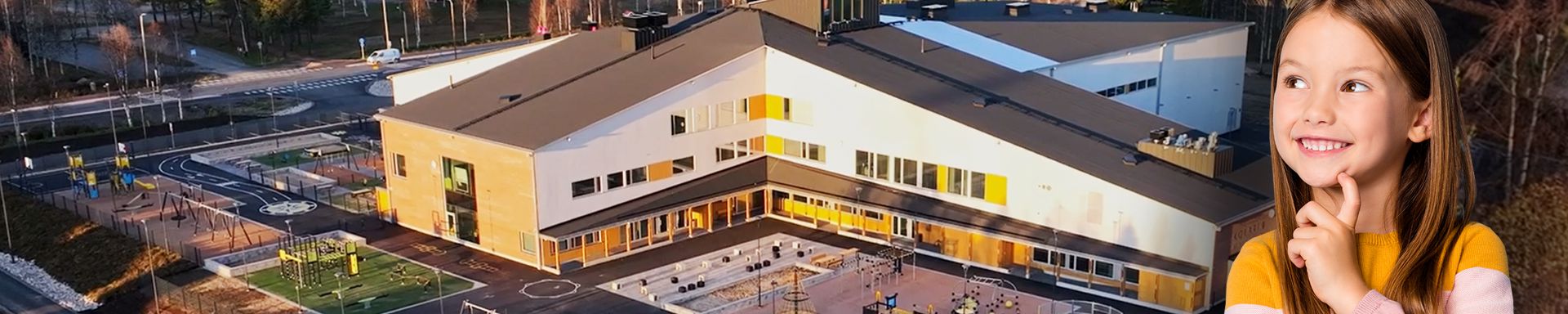 Kuvassa on suuri, moderni koulurakennus, jonka edessä on leikkikenttä ja urheilukenttä. Rakennuksen ympärillä on metsää ja taustalla näkyy laaja metsämaisema. Kuvan etualalla on lapsi, joka hymyilee ja katsoo ylöspäin mietteliäänä.