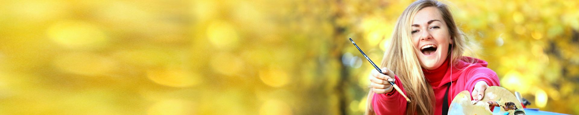 Henkilö pitää kädessään sivellintä ja palettia, jossa on eri värisiä maaleja. Tausta on epätarkka ja keltasävyinen, viitaten ulkoilmaympäristöön, jossa auringonvalo siivilöityy kasvillisuuden läpi. Henkilöllä on punainen vaate ja hän on keskittynyt maalaamiseen.