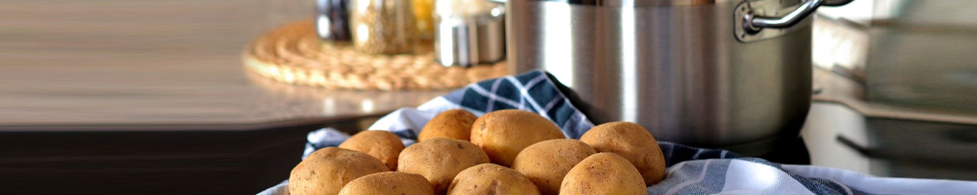 Kuvassa etualalla kuoripäällisiä perunoita. Taustalla teräskattila keittiö ympäristössä.