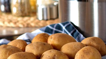 Kuvassa etualalla kuoripäällisiä perunoita. Taustalla teräskattila keittiö ympäristössä.