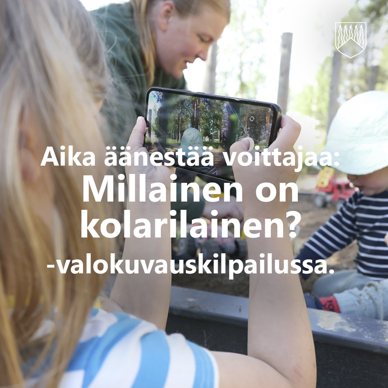 Lapsi ottamassa kännykällä kuvaa hiekkalaatikolla leikkivästä äidistä ja pikkuveljestä.