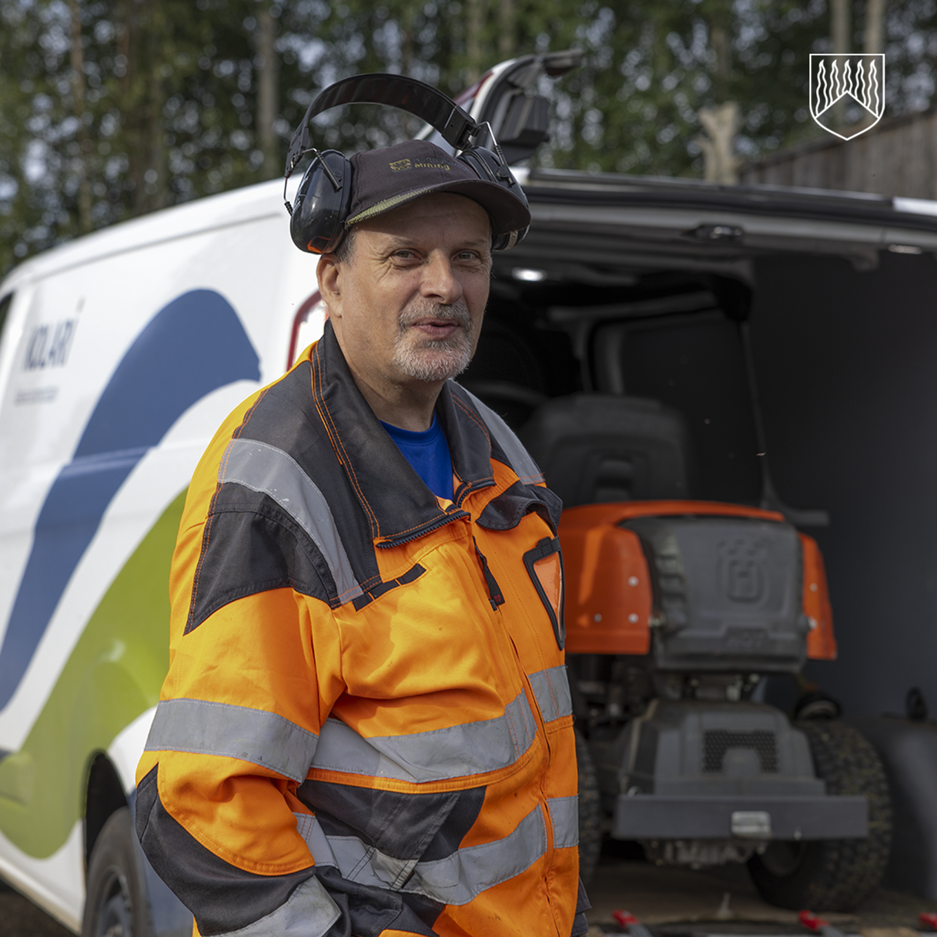 Kuvassa kotitalkkari Kimmo Nenämaa ajettavan ruohonleikkurin ja kunnan pakettiauton kanssa.