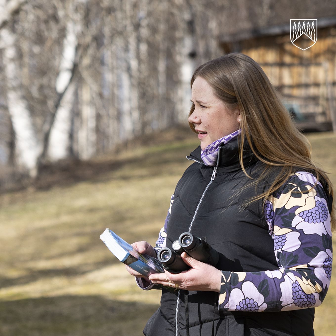 Nina-Maria omassa pihapiirissä matkalla joen rantaan bongaamaan lintuja kädessään kiikari ja lintukirja.