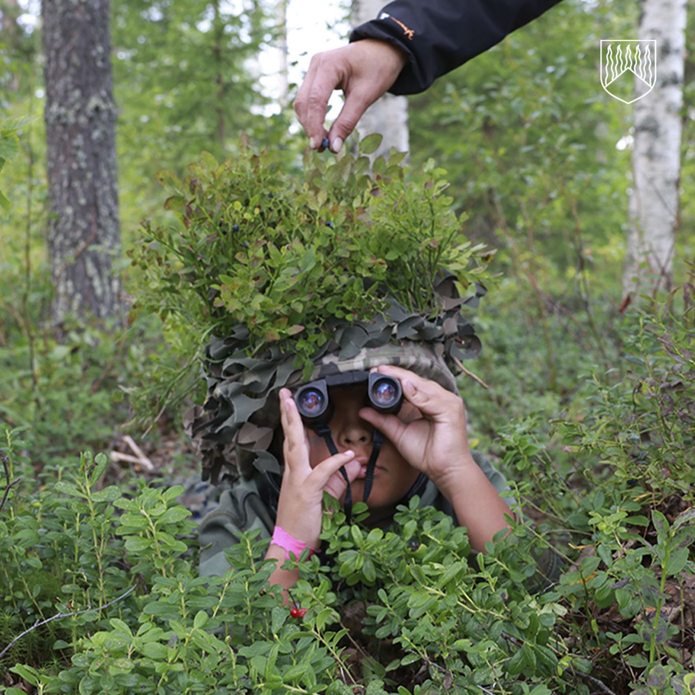 Kuvassa poika maastoutuneena metsään.