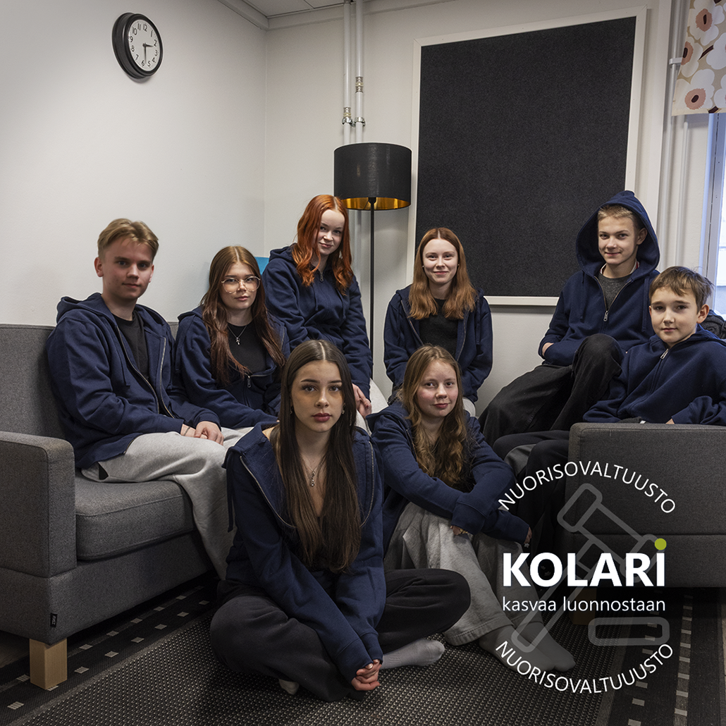 Ryhmä nuoria istuu rennosti sohvilla ja nojatuoleilla sisätilassa, jossa on vaalea seinä, seinäkello, lattiavalaisin ja suuri akustiikkapaneeli. Kaikilla on tummansiniset hupparit. Kuvan oikeassa alakulmassa näkyy Kolarin nuorisovaltuuston logo sekä teksti ”Kolari – kasvaa luonnostaan”.