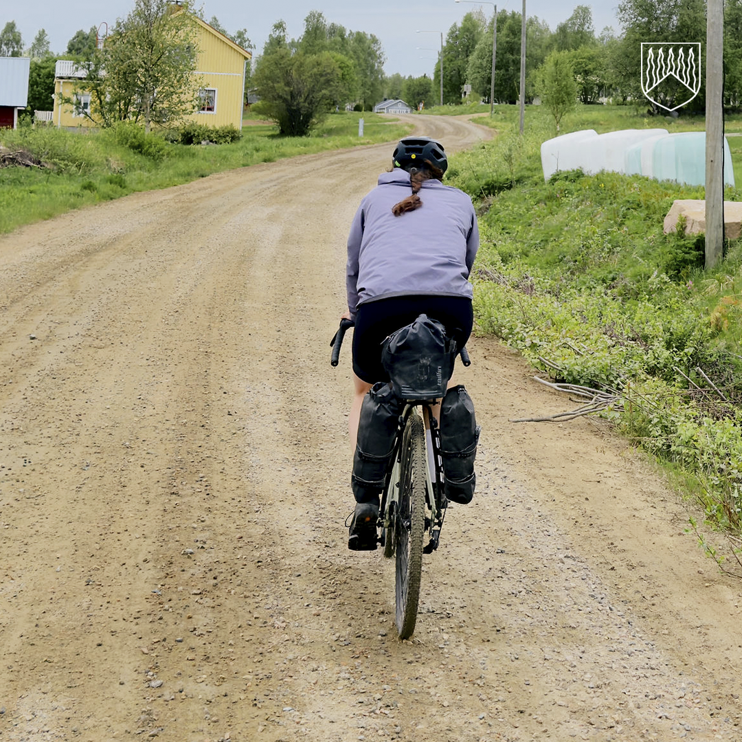 Retkipyöräilijä polkee Kolarin järvikylien soratiellä vehreän maalaismaiseman halki.