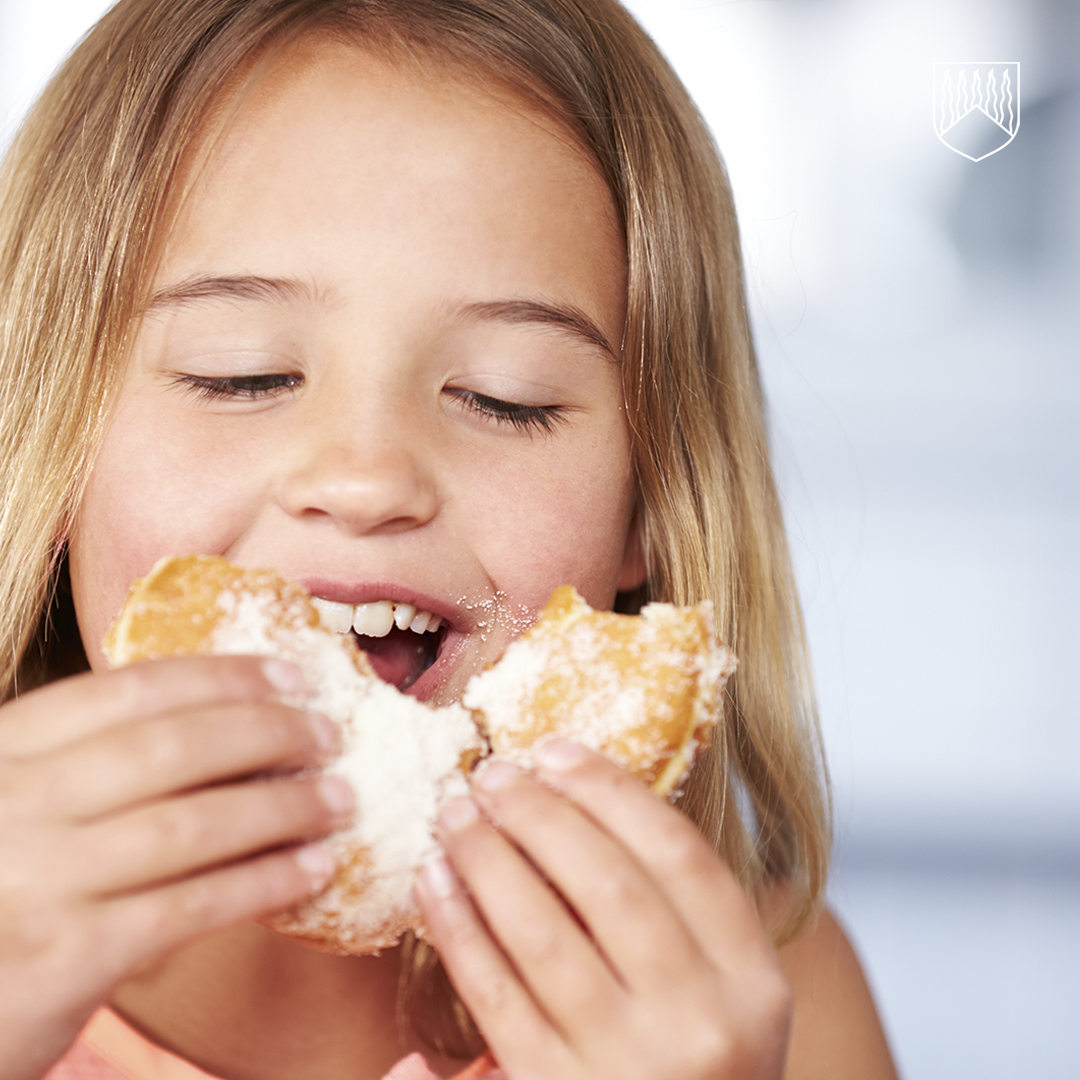 Lapsi pitää käsissään sokerilla kuorrutettua leivonnaista ja syö sitä.